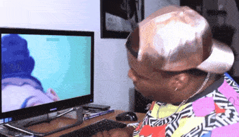 a man wearing a hat looks at a computer monitor