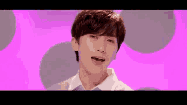 a young man is standing in front of a pink background .