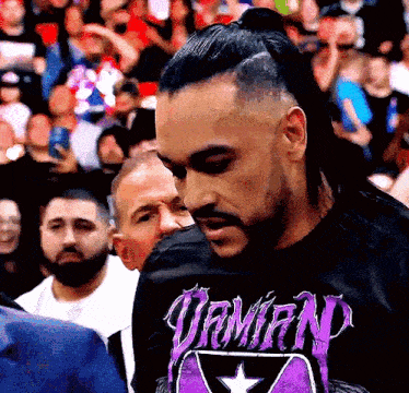a man wearing a black shirt with a purple logo that says damian
