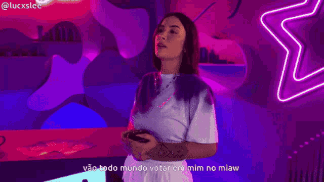 a woman in a tie dye shirt is holding a video game controller in front of a neon sign that says luckslee