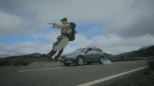 a man with a backpack is jumping in the air in front of a volvo suv