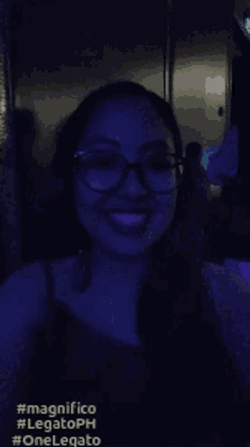 a woman wearing glasses is smiling in a dark room with the words magnifico on the bottom