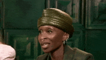 a woman wearing a green hat and earrings is standing next to another woman .