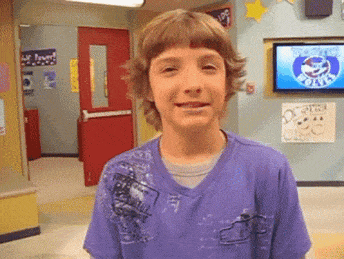 a young boy wearing a purple shirt is smiling in front of a tv that says ' shark tank ' on it