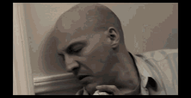 a bald man is leaning against a wall while holding a napkin
