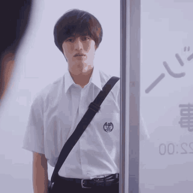a young man in a school uniform is standing in front of a glass door with chinese writing on it .