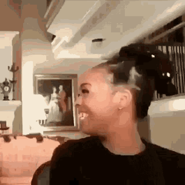 a woman is smiling in a living room with a picture on the wall behind her .