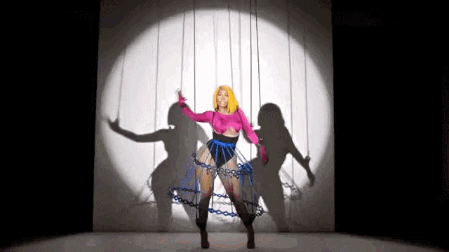 a woman in a pink top and blue skirt is dancing on a stage with chains around her waist .
