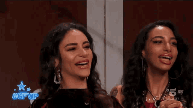 two women are laughing in front of a tv screen that says #gfvip