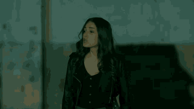 a woman in a black leather jacket stands in a dark room
