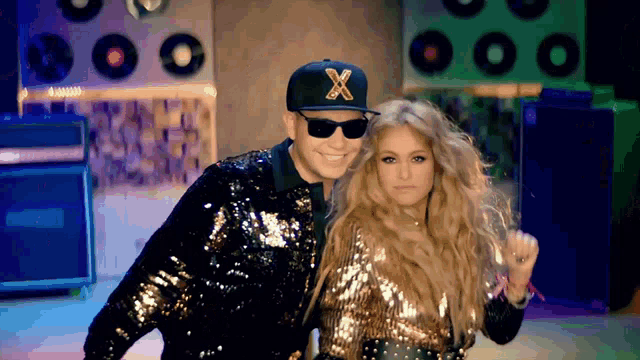 a man and a woman are posing for a picture and the man is wearing a hat with the letter x on it