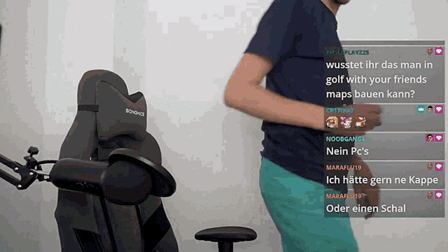 a man in a blue shirt is standing in front of a gaming chair with a screenshot of a stream on the screen
