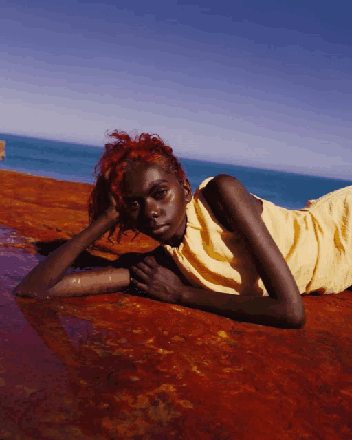 a woman with red hair is laying on a red surface in front of the ocean