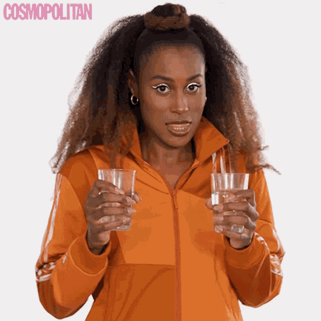 a woman in an orange jacket is holding two glasses of water in front of a cosmopolitan logo