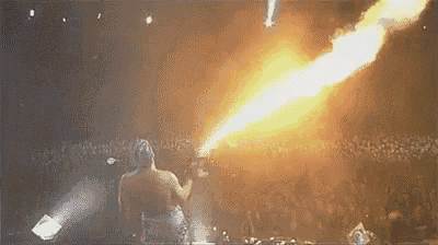 a man is holding a torch in front of a crowd while a fire is coming out of his mouth .