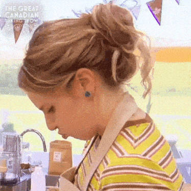 a woman is standing in a kitchen wearing an apron and a striped shirt and looking down .
