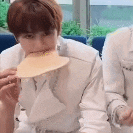 a man in a white suit is eating a pancake with his mouth .