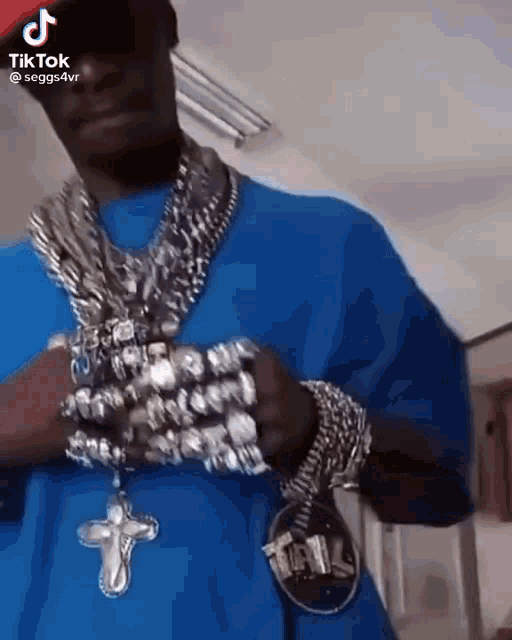 a man in a blue shirt is wearing a lot of jewelry and a cross necklace .