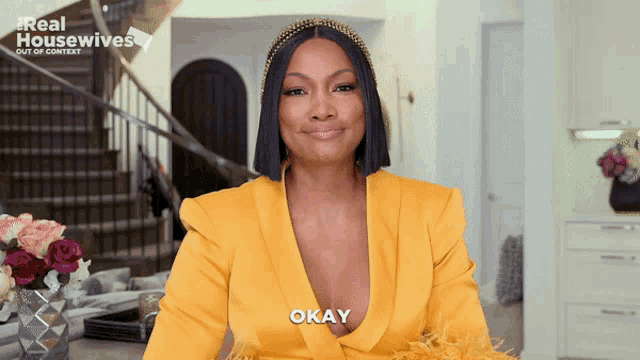 a woman in a yellow jacket says okay in front of a sign that says real housewives