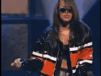 a woman wearing sunglasses and a leather jacket is standing on a stage in front of a spotlight .