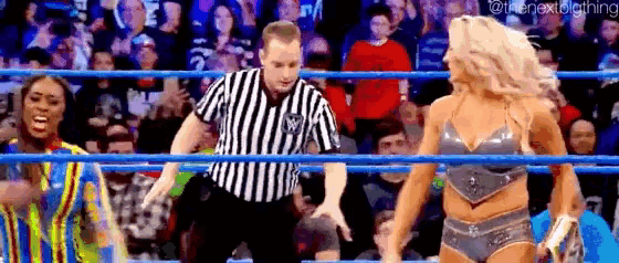 a referee is standing in the middle of a wrestling ring between two women .
