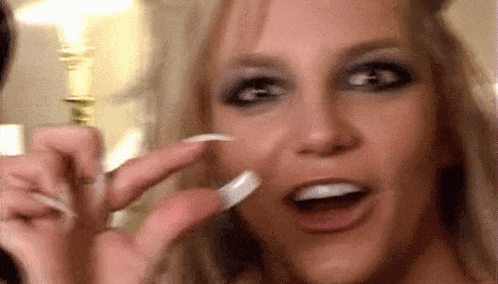 a close up of a woman 's face with long nails and a ring on her finger .