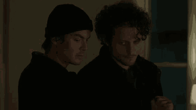 a couple of men standing next to each other in a dark room .