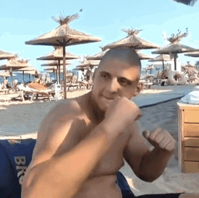 a shirtless man sitting on a beach wearing a pair of black shorts that say bkc