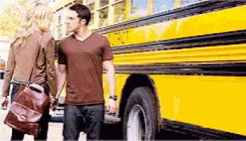 a man and woman are holding hands in front of a yellow school bus