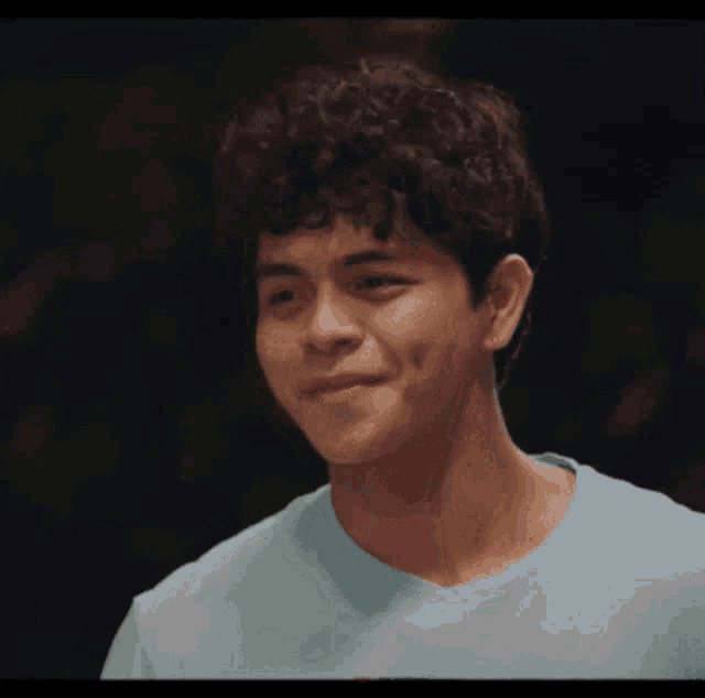 a young man with curly hair is wearing a light blue shirt and making a funny face .