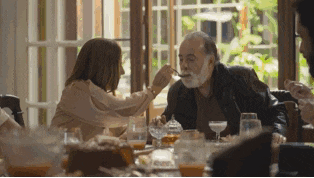 a woman is feeding an older man with a spoon at a dinner table