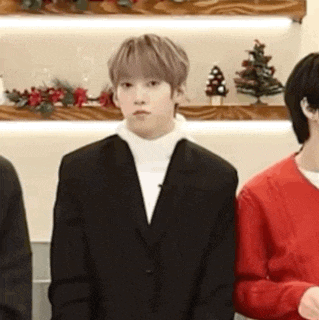 a man in a suit and white turtleneck is standing in front of a shelf with christmas trees .