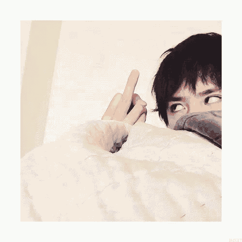 a person laying on a bed with their face covered with a blanket and giving the middle finger