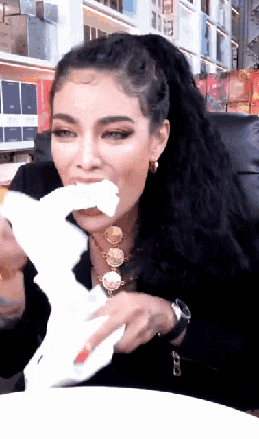 a woman wearing a watch and a necklace is eating a piece of paper
