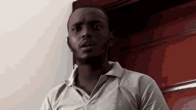 a man in a white shirt is standing in front of a wooden door and looking at the camera .