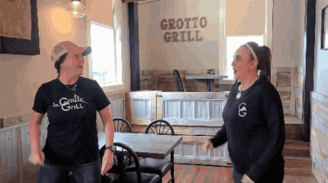 two women dancing in front of a grotto grill sign