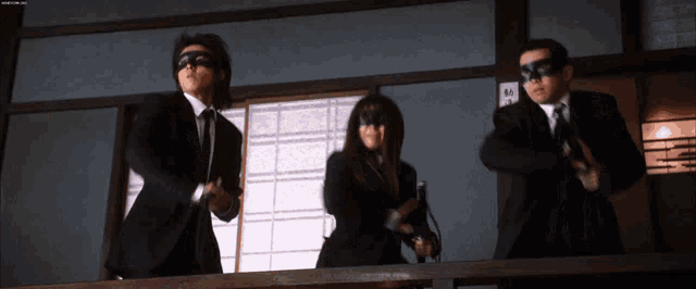 a man in a suit and tie is standing next to a woman in a mask and holding a gun