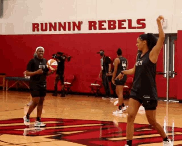 a group of female basketball players are practicing in front of a wall that says runnin ' rebels
