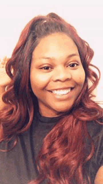 a woman with long red hair is smiling for the camera while wearing a black shirt .