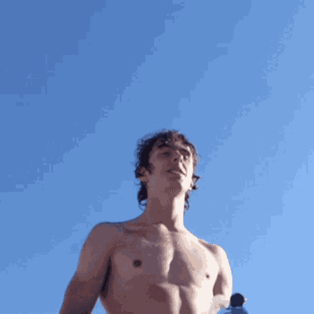 a shirtless young man with wet hair looks up at the sky