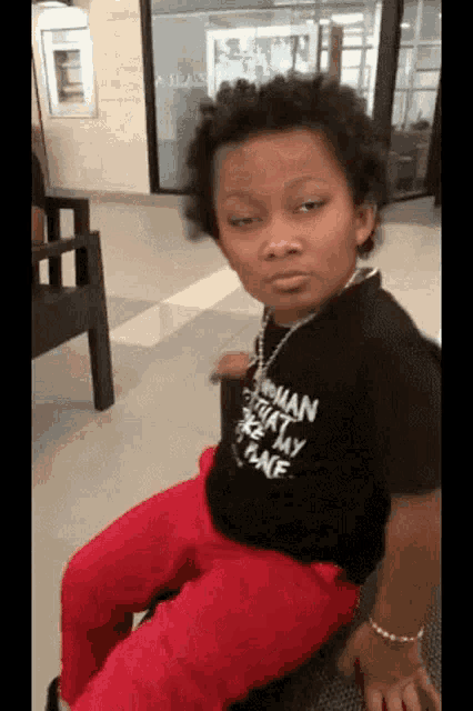 a young boy wearing a black shirt that says woman on it is sitting on a chair