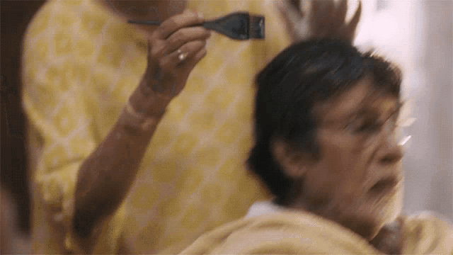 a woman is applying hair dye to a man 's head
