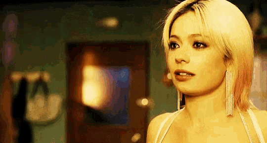 a woman with blonde hair and earrings is standing in front of a door in a room .