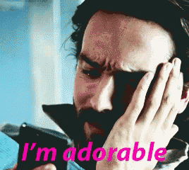 a man with a beard holds his hand to his face and says i 'm adorable in pink letters