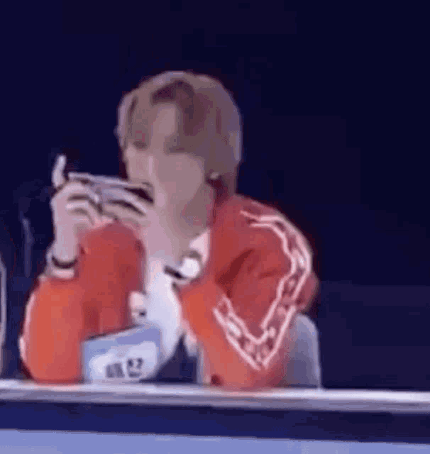 a man in a red jacket is sitting at a table holding a cell phone in his hands .