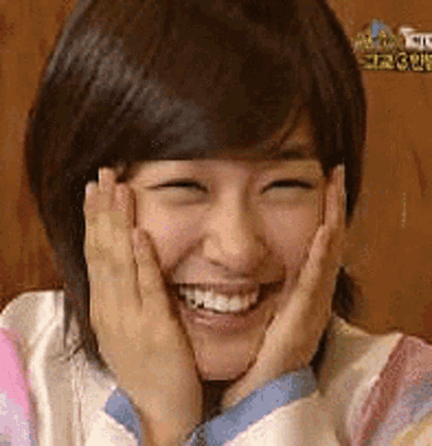 a woman is smiling and holding her face with her hands .