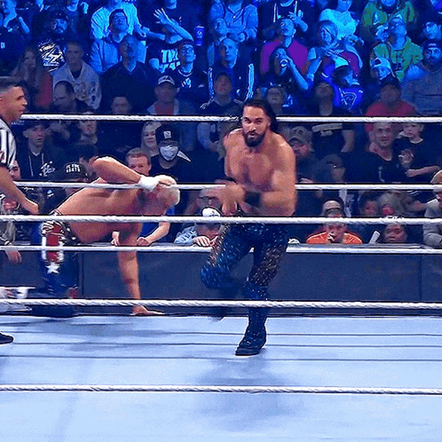 a wrestler in a ring with a referee and a crowd behind him wearing a shirt that says tna