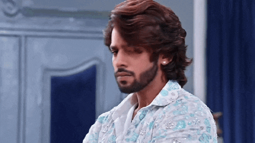 a man with a beard and long hair is wearing earrings and a blue shirt .