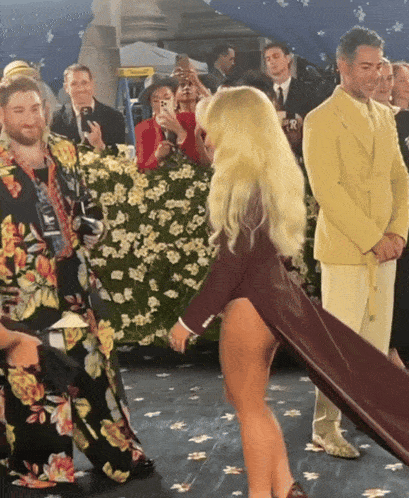 a group of people are standing around a woman in a high slit dress
