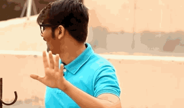 a man wearing glasses and a blue shirt is waving his hand .